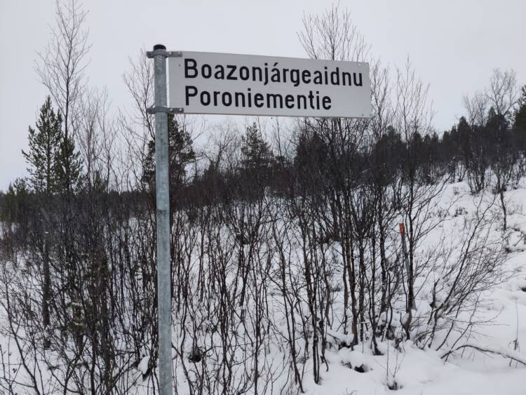 Talvisen vesaikon edessä tiennimikyltti, jossa lukee pohjoissaameksi Boazonjárgeaidnu ja suomeksi Poroniementie.