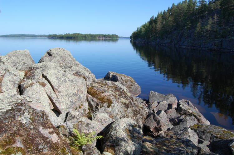 Kivinen niemenkärki, kallioista rantaa ja kesäinen tyyni järvenselkä, jossa näkyy saariryhmä.